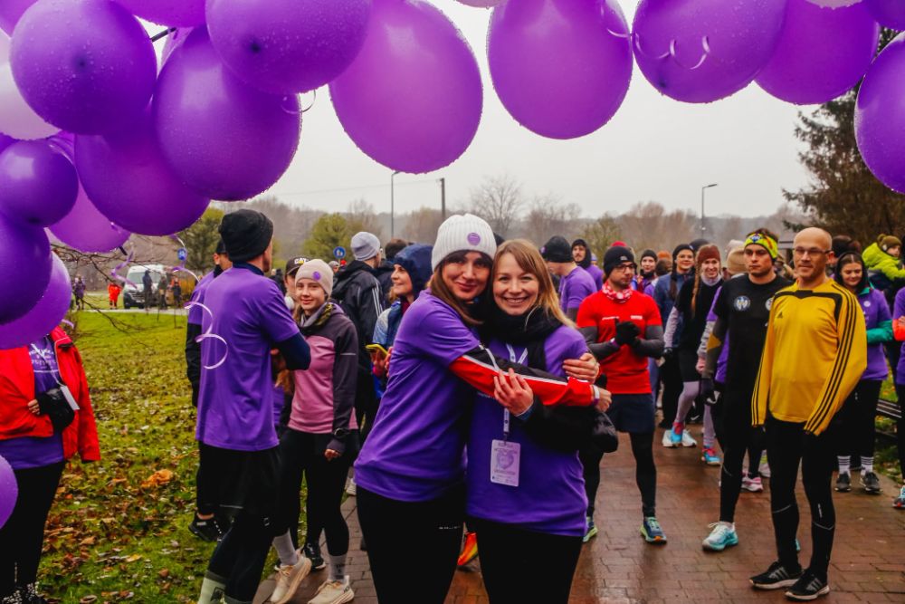 Dwie uczestniczki w fioletowych koszulkach ściskają się pod balonami
